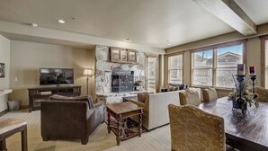 A living room with a stone fireplace, a television, and a dining area with a table and chairs. - Mont Cervin by Avantstay Condo w/ Hot Tub + Jetted Tub + Fireplace Ski-in/ski-out (Park City)