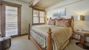 A bedroom with a large bed, wooden headboard, two windows with blinds, a bedside table with a lamp, and a painting on the wall. - Mont Cervin by Avantstay Condo w/ Hot Tub + Jetted Tub + Fireplace Ski-in/ski-out (Park City)