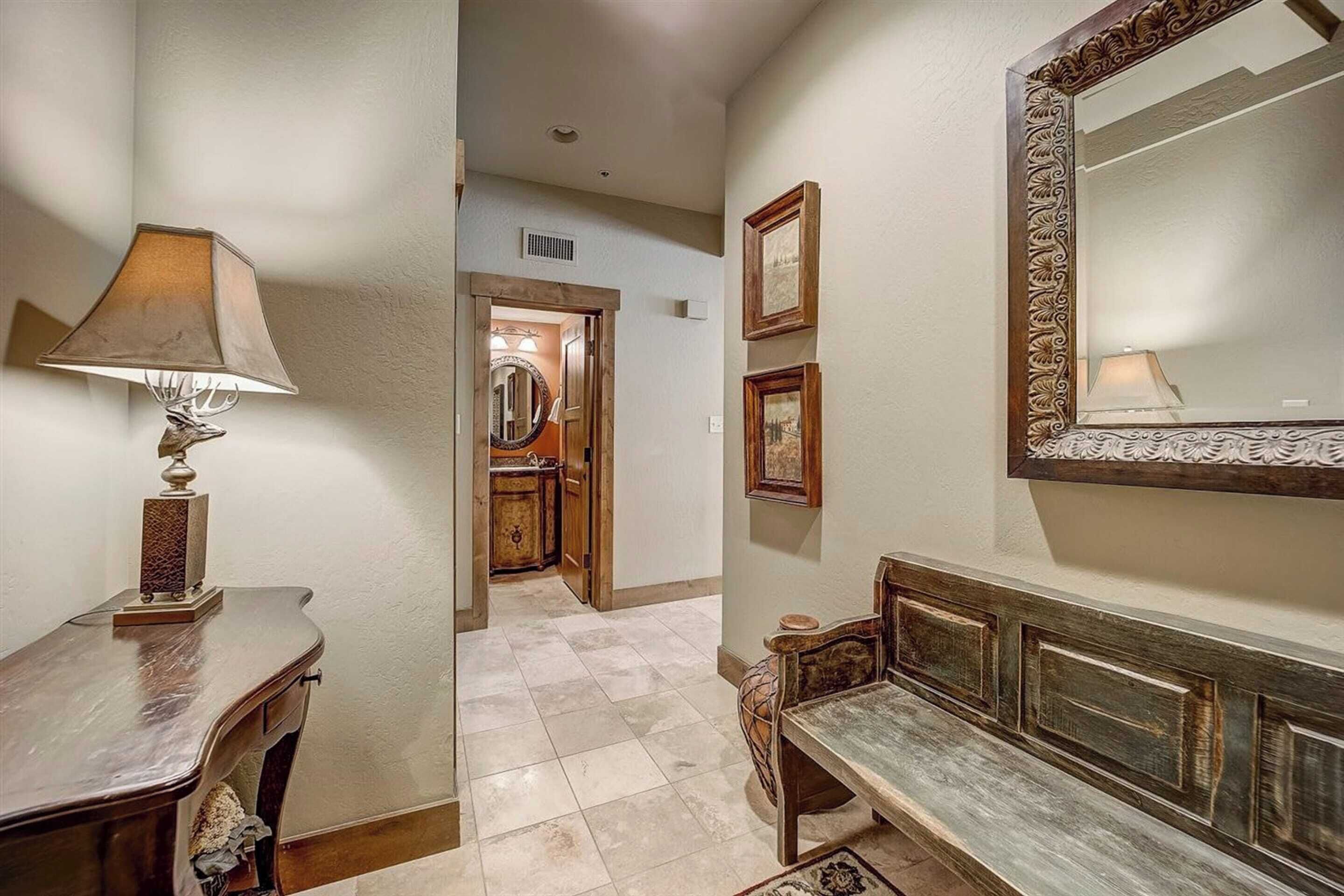 A hallway with a lamp, a bench, and a mirror.