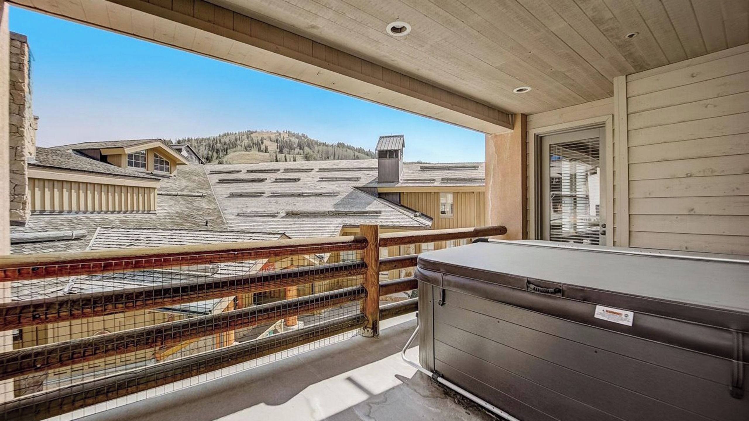 A room with a view of a ski resort, a hot tub, and a wooden railing.
