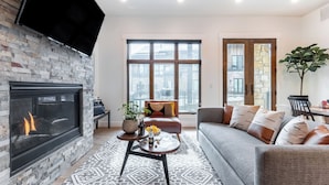 A modern living room with a fireplace, a sofa, a coffee table, and a large window with a city view. - Kokopelli by Avantstay Close to the Ski Slopes in This Majestic Home in Park City (Park City)