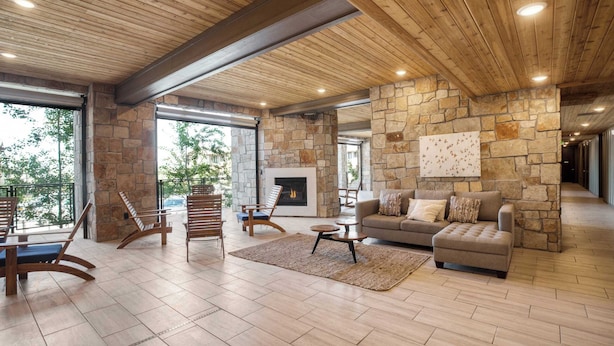 A spacious living area with a stone fireplace, wooden ceiling beams, and a view of greenery outside. - Kokopelli by Avantstay Close to the Ski Slopes in This Majestic Home in Park City (Park City)