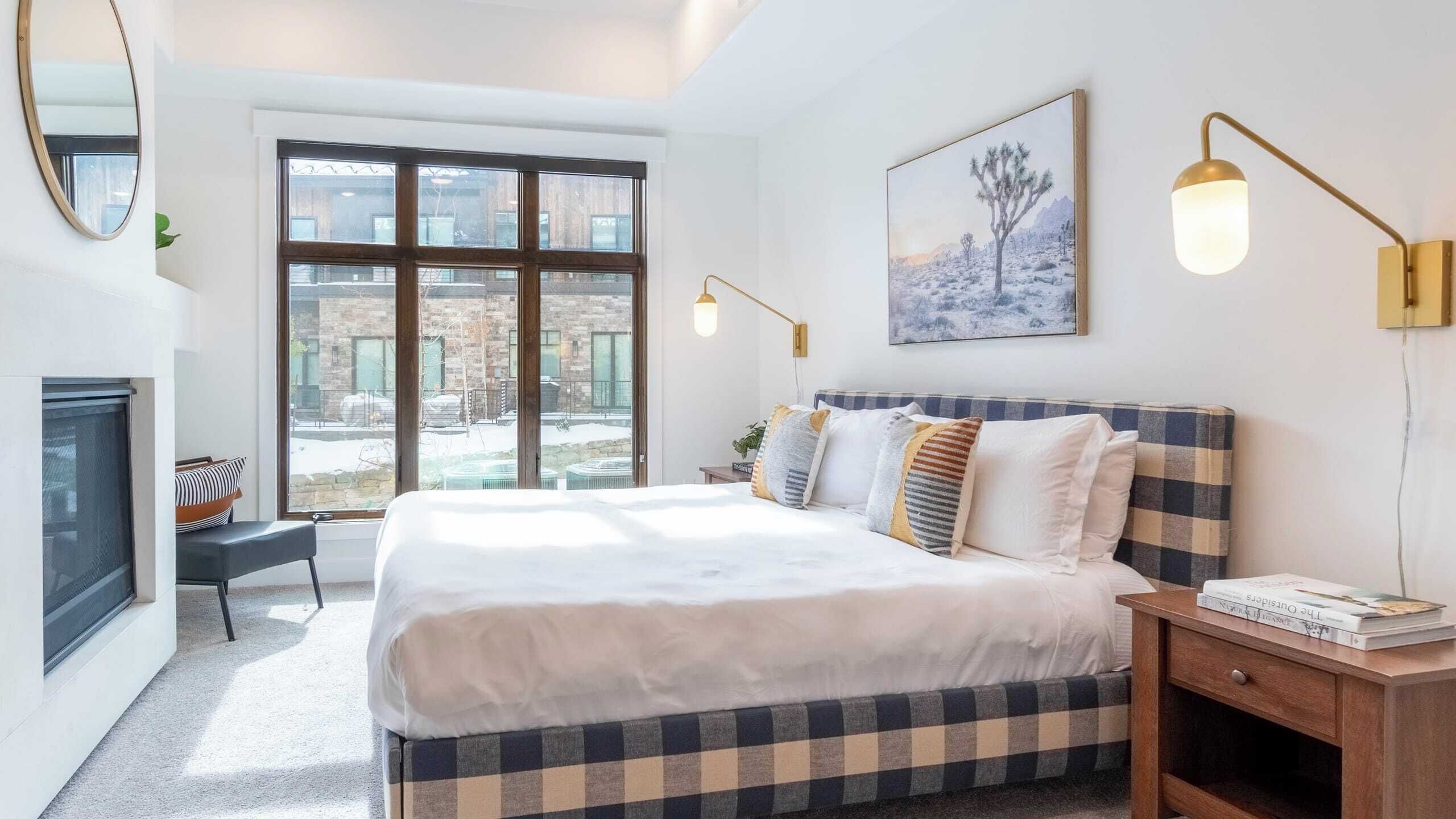Una camera da letto moderna con un letto grande, un comodino, una libreria, un caminetto e un'ampia finestra con vista sull'esterno.