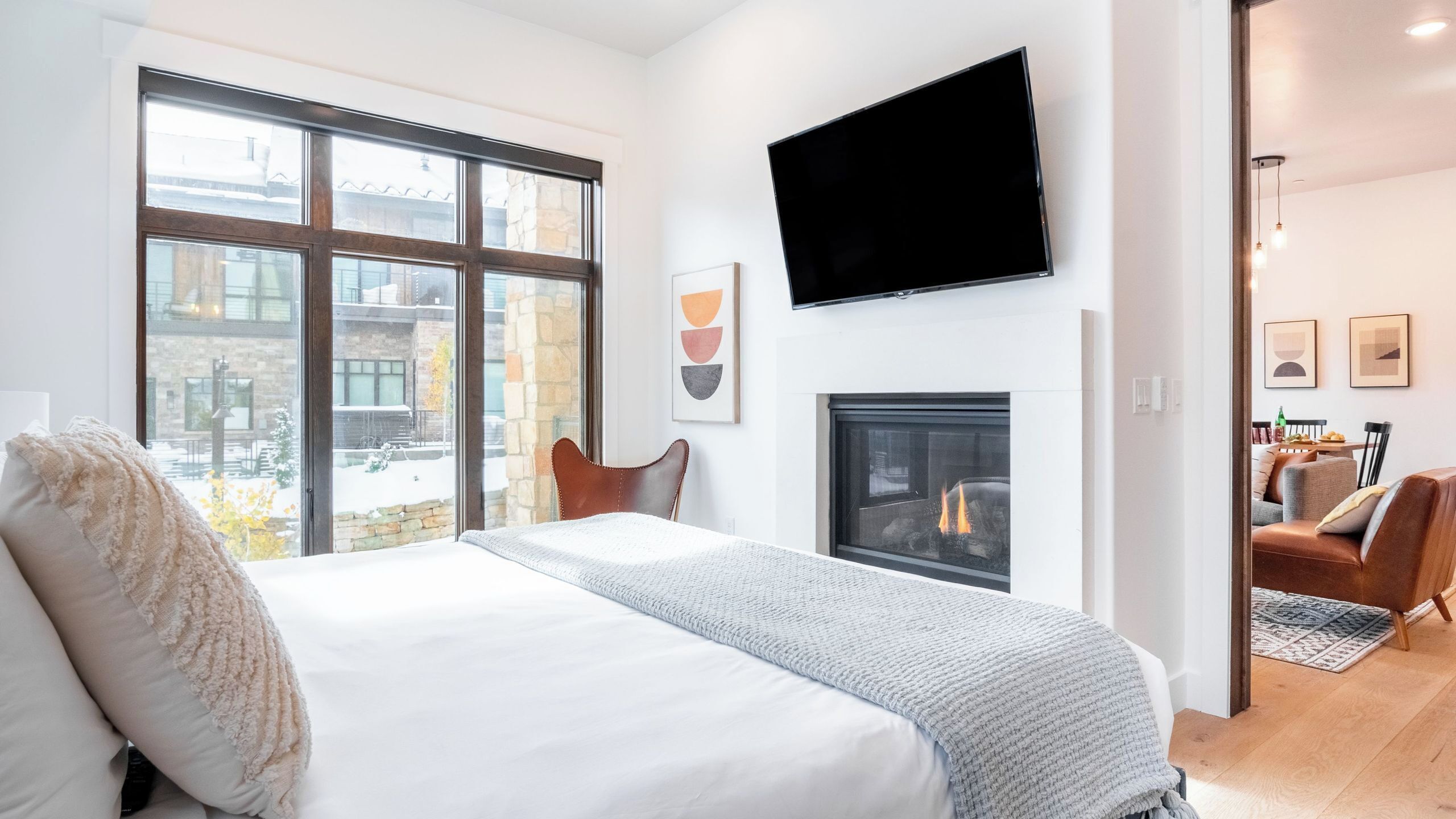 A modern hotel room with a large bed, a fireplace, a TV mounted on the wall, and a view of the outside.