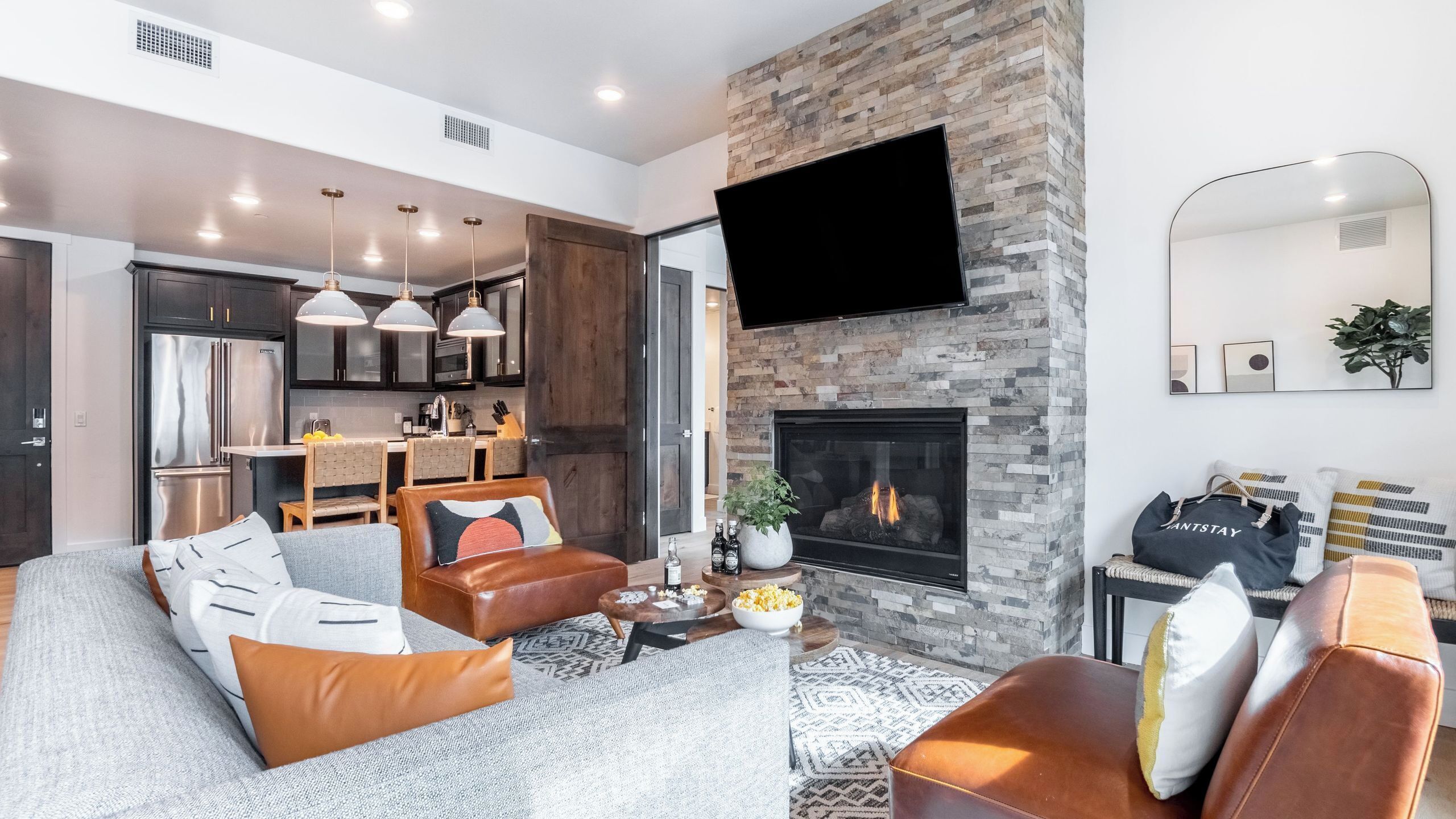 Una sala de estar moderna con chimenea, sofás de cuero, una mesa de centro y una cocina al fondo.