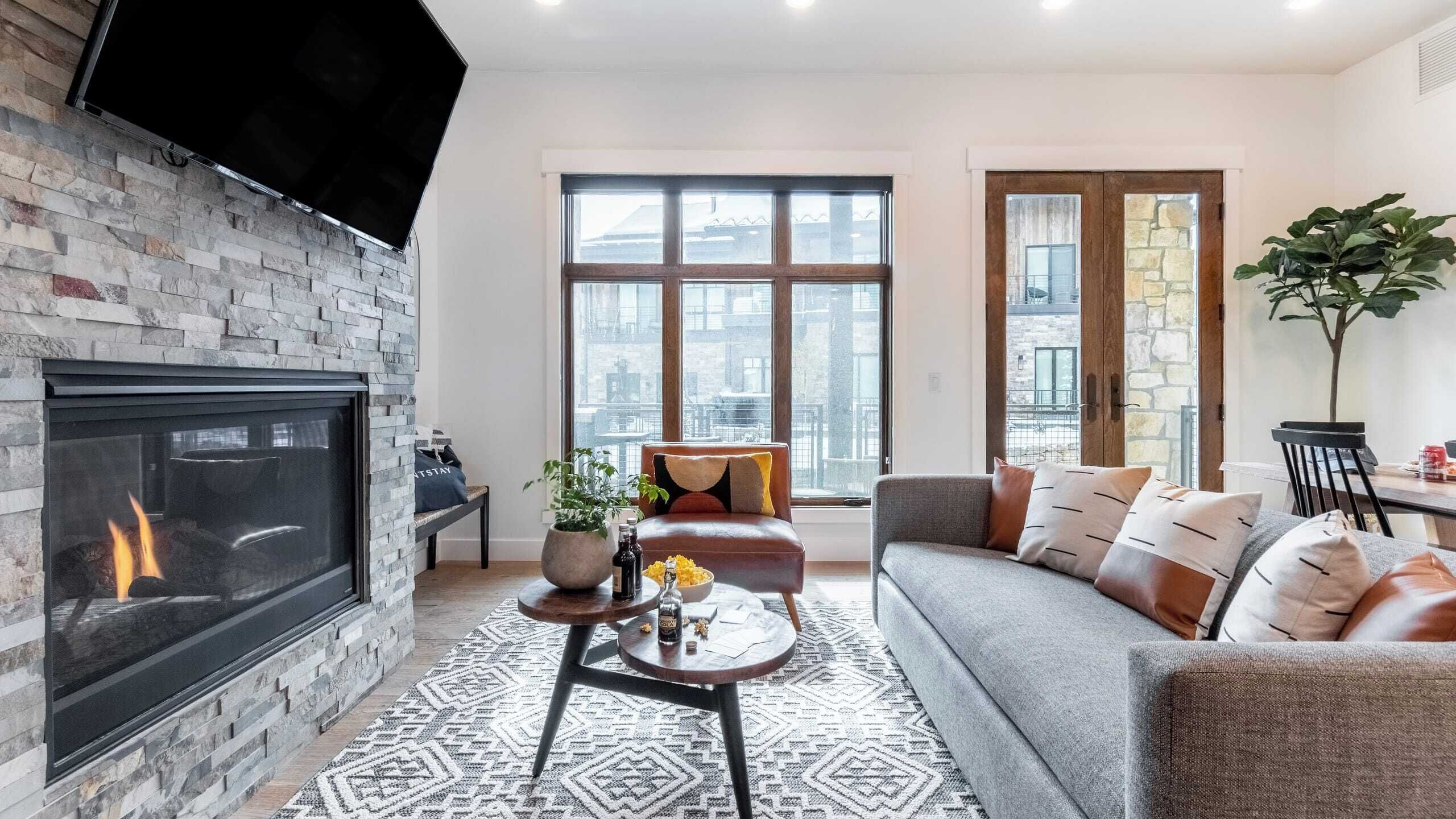 A modern living room with a fireplace, large windows, a sofa, and a coffee table.