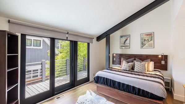 A bedroom with a large sliding glass door leading to a deck, a bed with patterned bedding, and two wall-mounted posters.