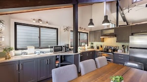 A modern kitchen with dark cabinets, stainless steel appliances, and a dining area with a wooden table and chairs.