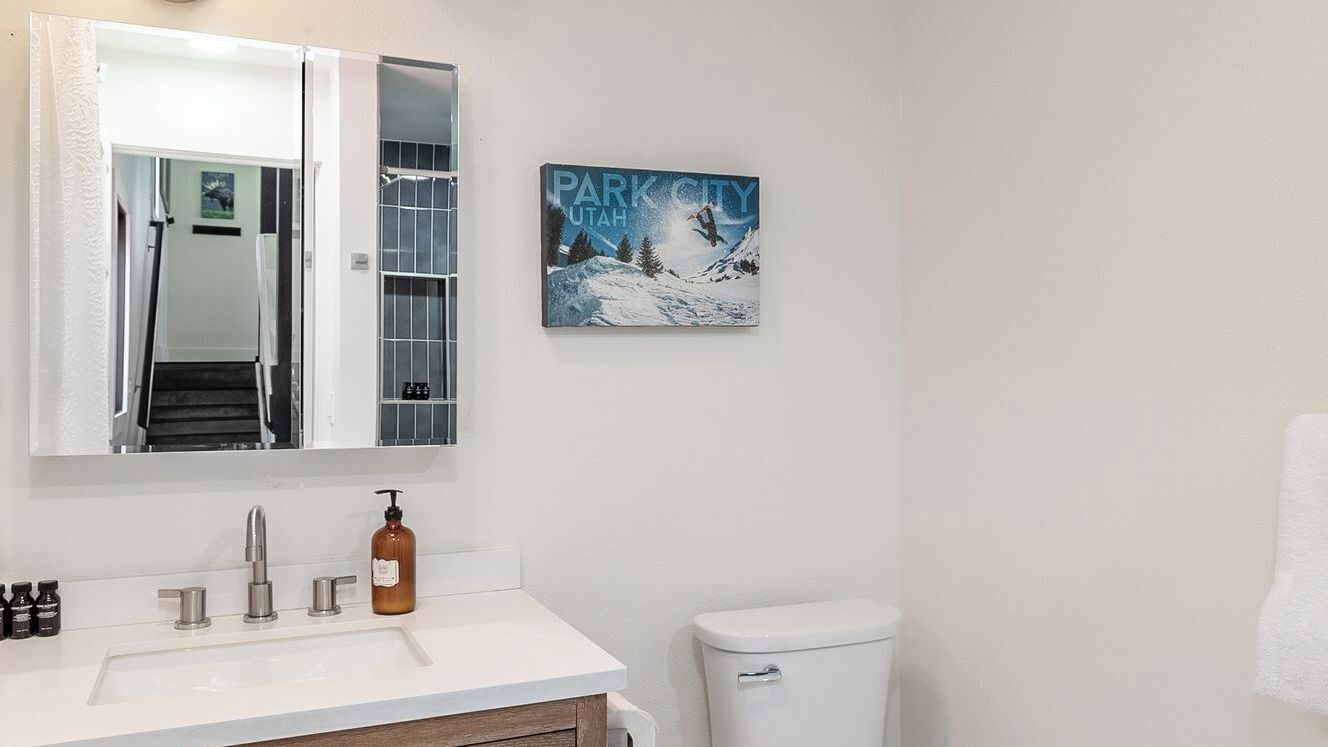 Een badkamer met een witte wastafel, een spiegel, een toilet en een lijst met een foto van een snowboarder in de bergen.