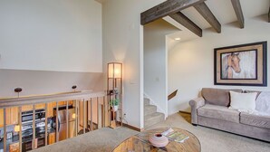 A living room with a sofa, a coffee table, a staircase, and a kitchen area with appliances. - Slope-side Townhome Steps to Main St, Deck View of Old Town Quittin Time Townhome by Avantstay (Park City)