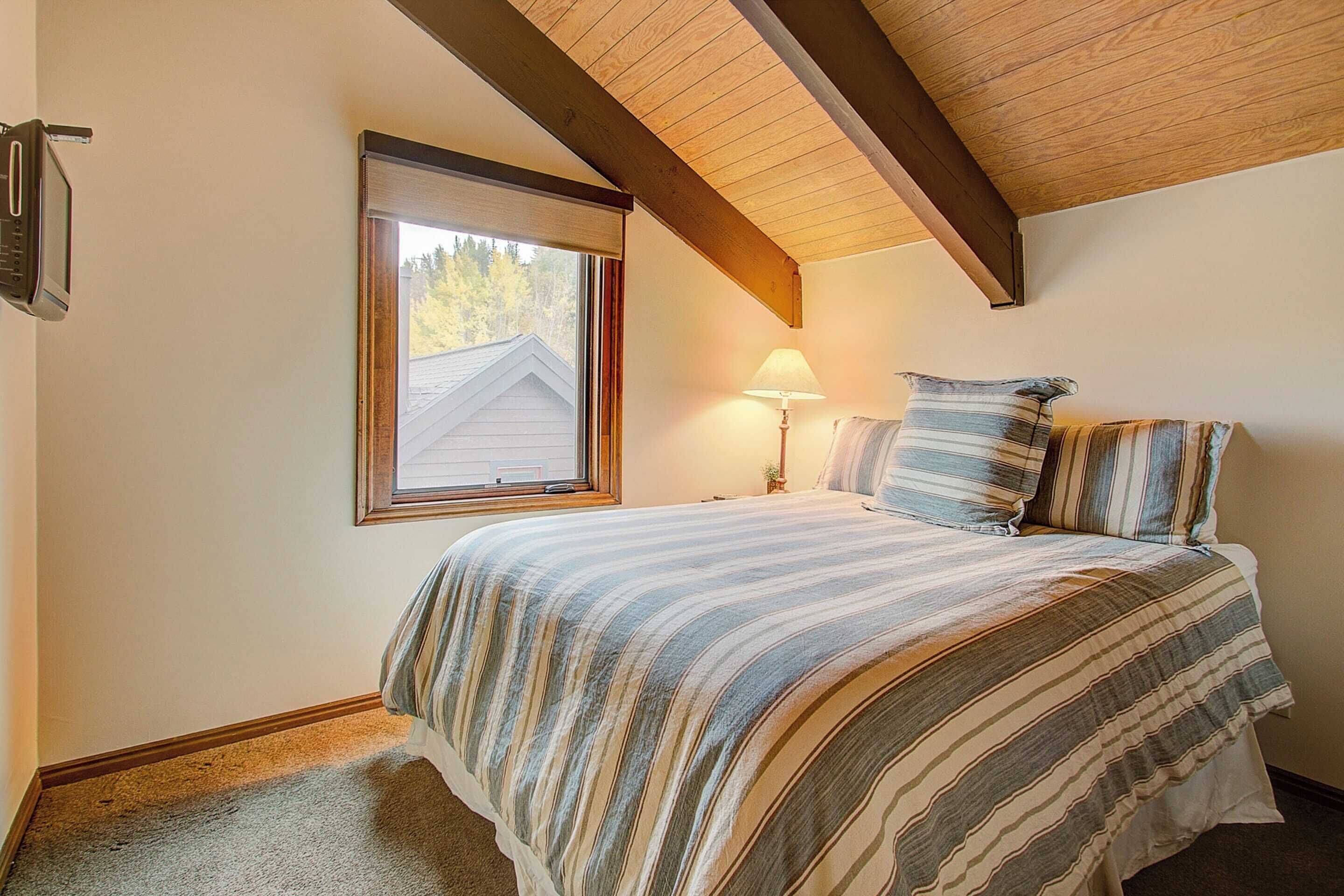 A bedroom with a bed, a window, a lamp, and a ceiling beam.