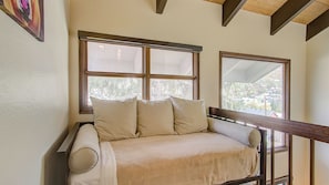 A room with a sofa bed, large windows, and wooden beams on the ceiling.