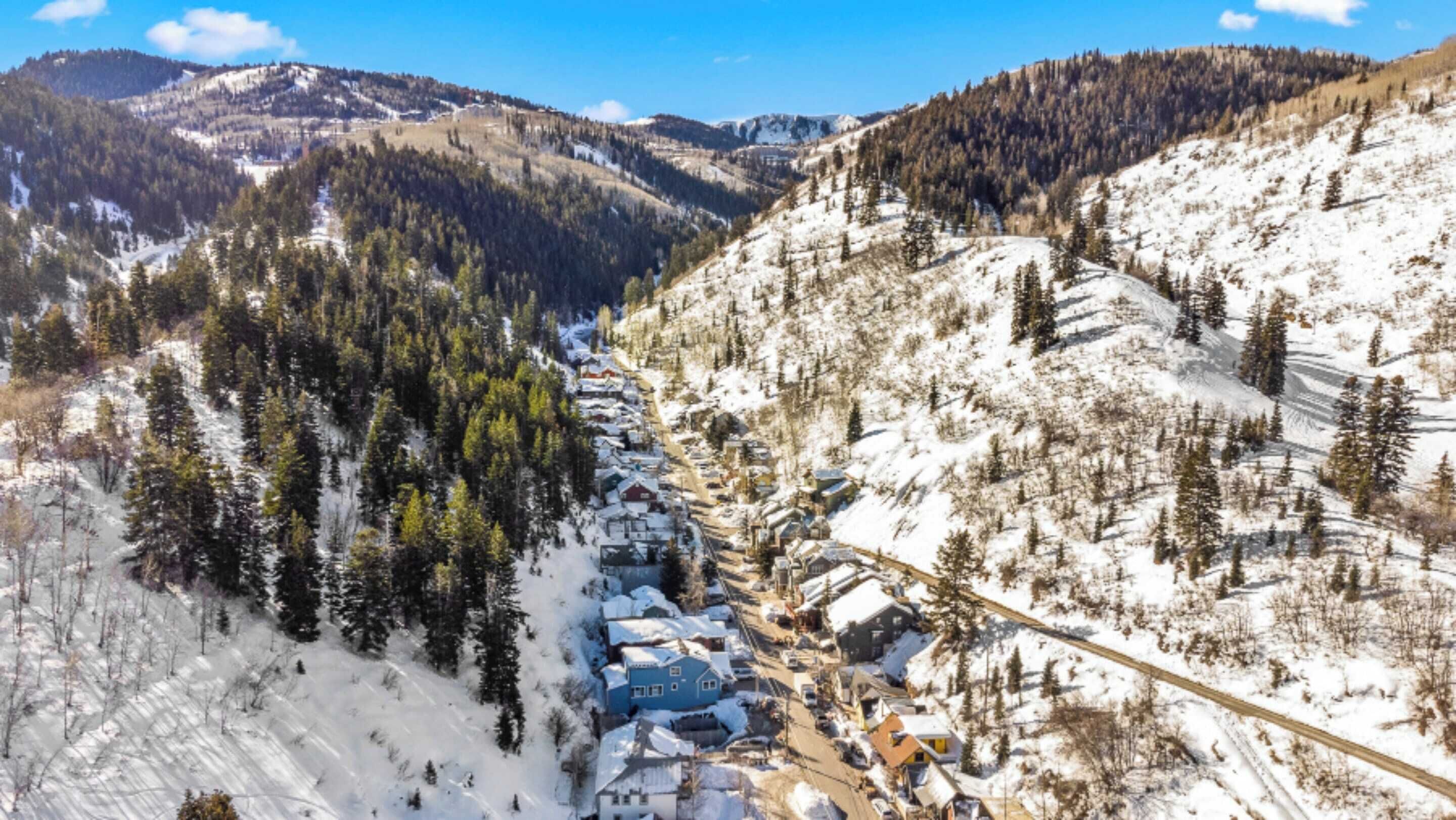 A snow-covered mountain village with a main road running through it, surrounded by dense forests and hills.
