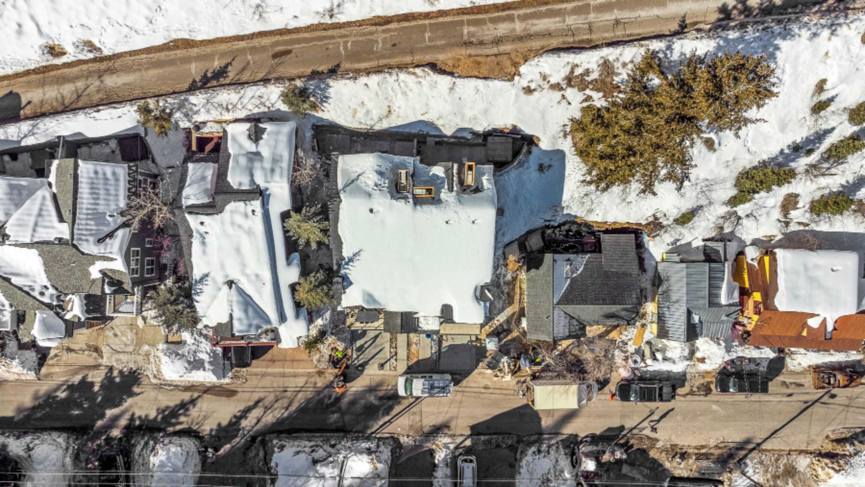 A residential area with houses partially covered in snow, some with visible roofs and chimneys, and a few trees.