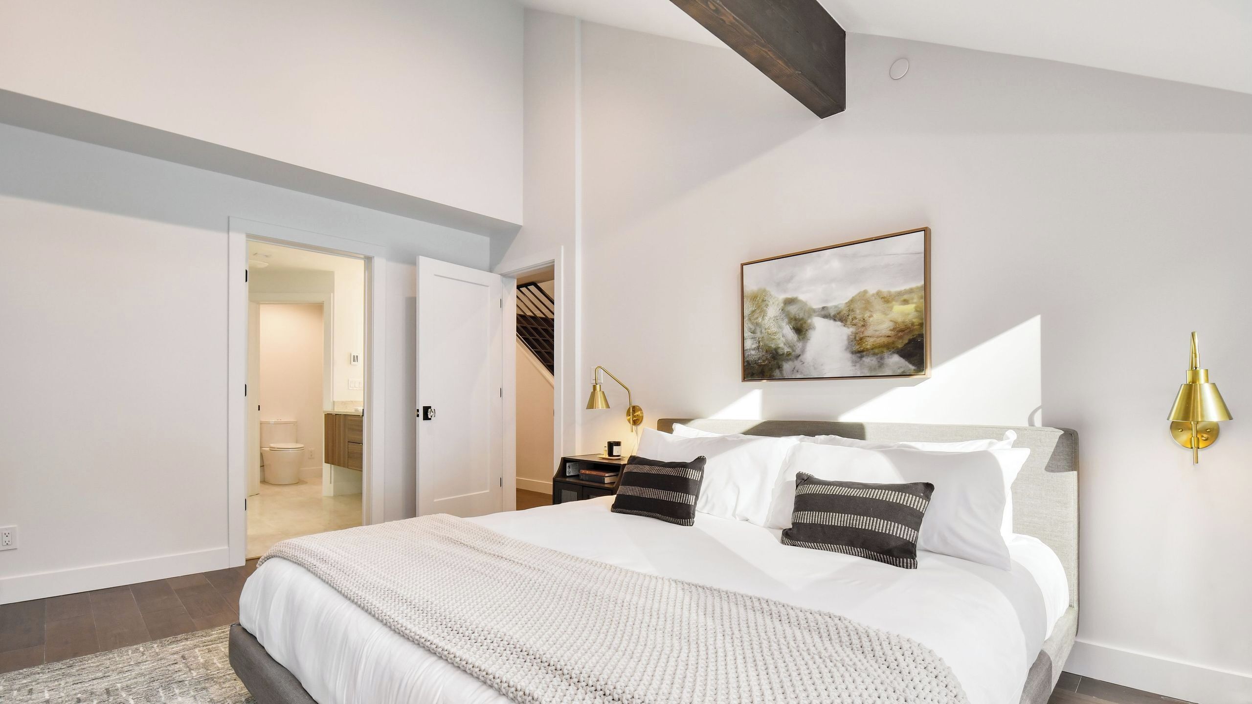 Un dormitorio con cama, mesita de noche, lámpara de pared y un cuadro.