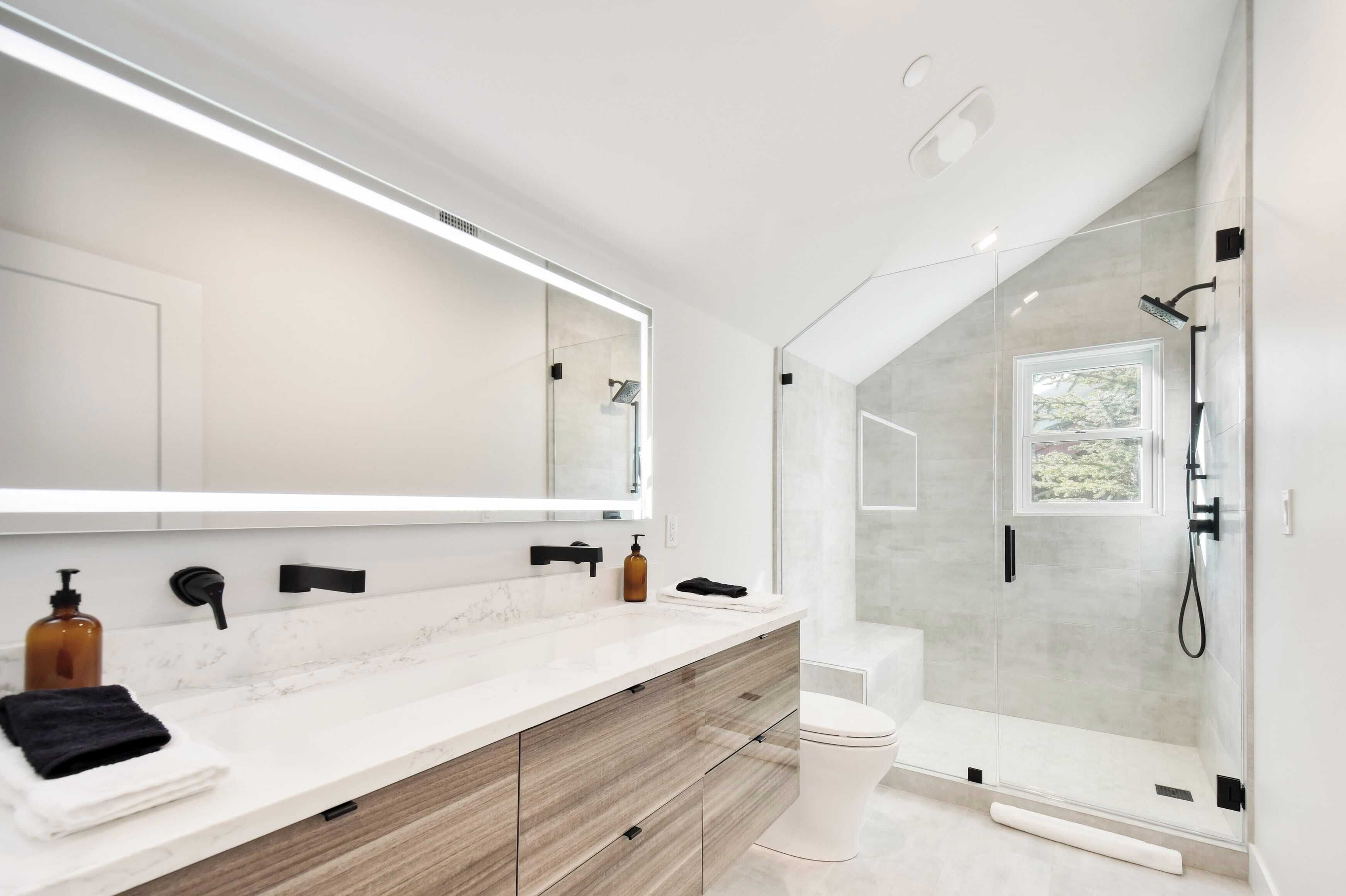 A modern bathroom with a large mirror, a marble countertop, a wooden cabinet, a toilet, and a glass-enclosed shower.