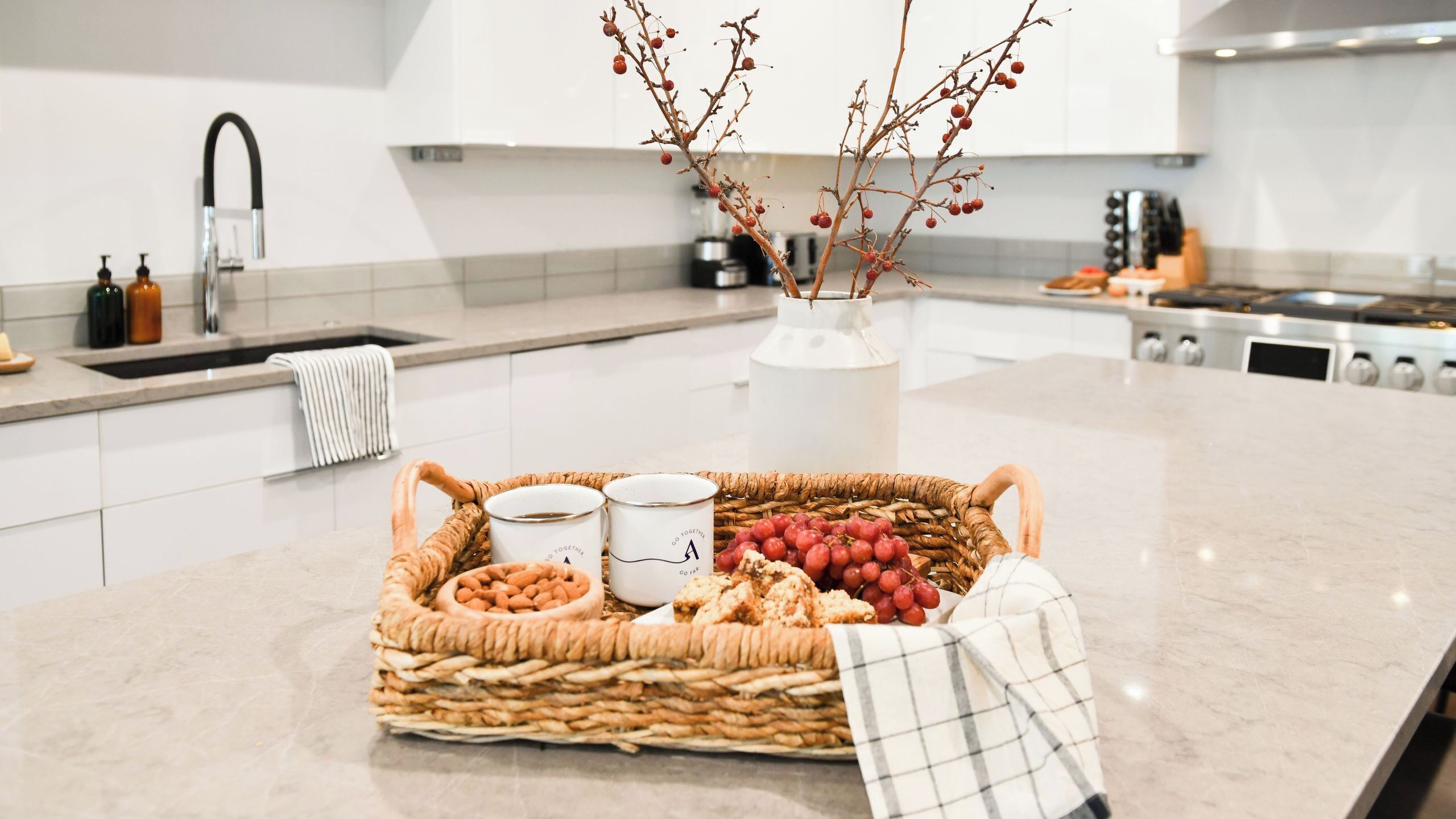 A kitchen with a marble countertop, a woven basket with snacks, a vase with branches, and a coffee maker.