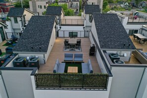 A rooftop patio with a wooden deck, outdoor seating, and a view of neighboring buildings.