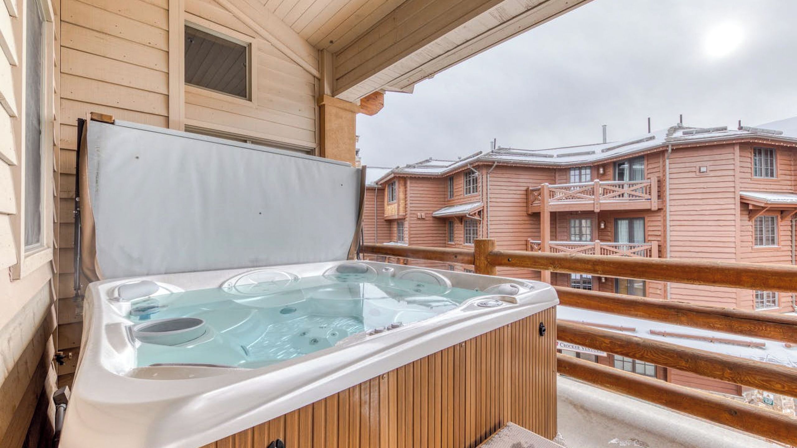 A wooden hot tub on a balcony with a view of wooden buildings.
