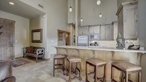 Una cucina con mobili in legno, un frigorifero, un forno a microonde e una macchina da caffè. Sono presenti tre sgabelli di legno al bancone.