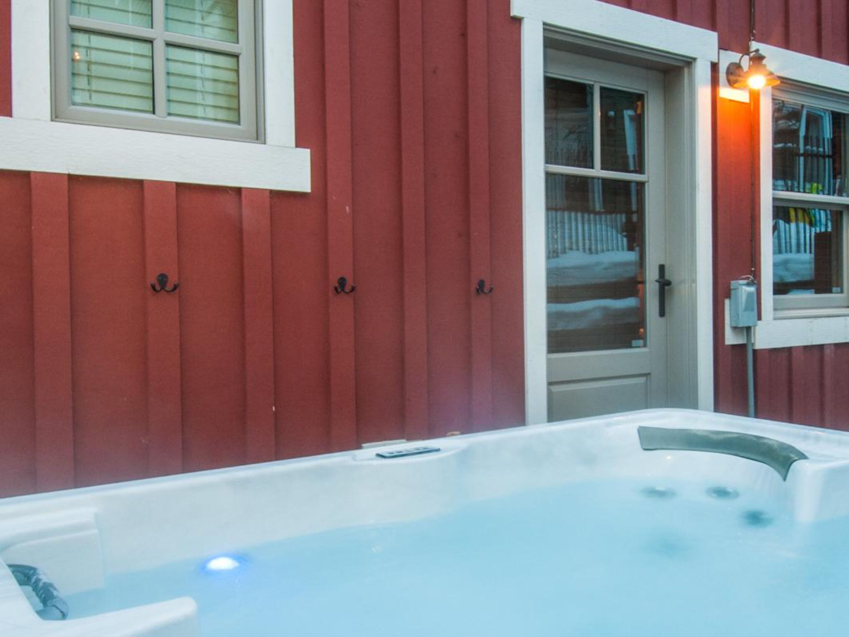 Een hottub naast een rood gebouw met een witte deur en ramen.