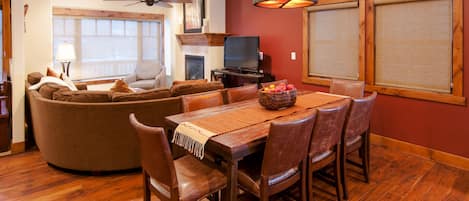 Una sala de estar con una mesa de comedor de madera, sillas de cuero, un sofá y un televisor.