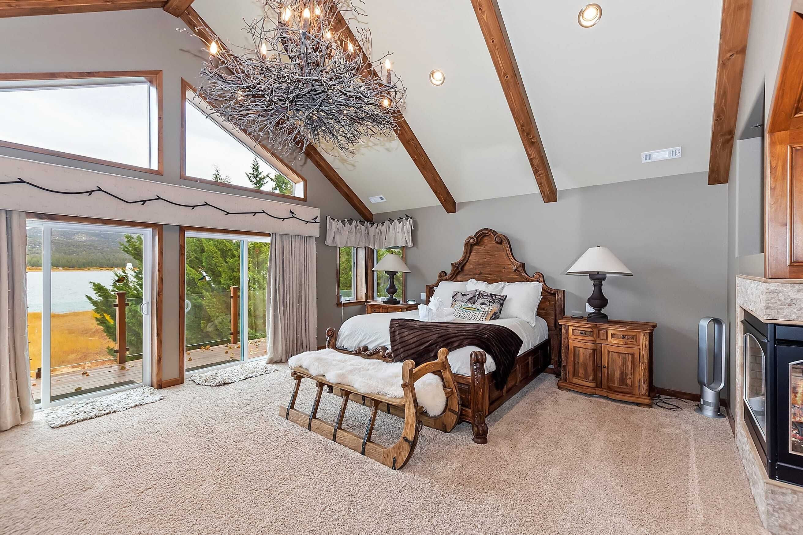 A bedroom with a large bed, a wooden bench, a chandelier, and a fireplace.