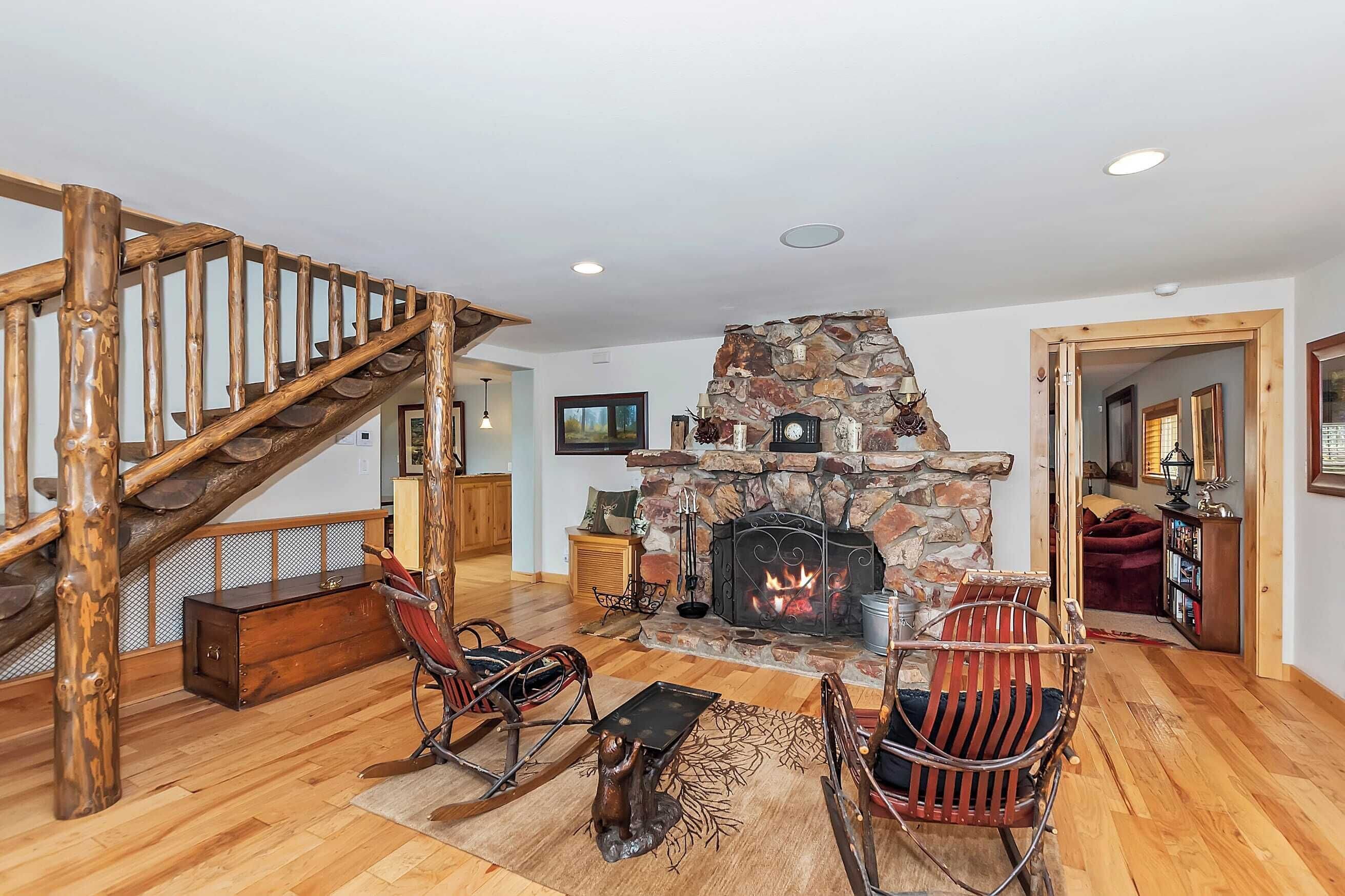 A spacious living room with a stone fireplace, wooden flooring, and a rustic staircase.