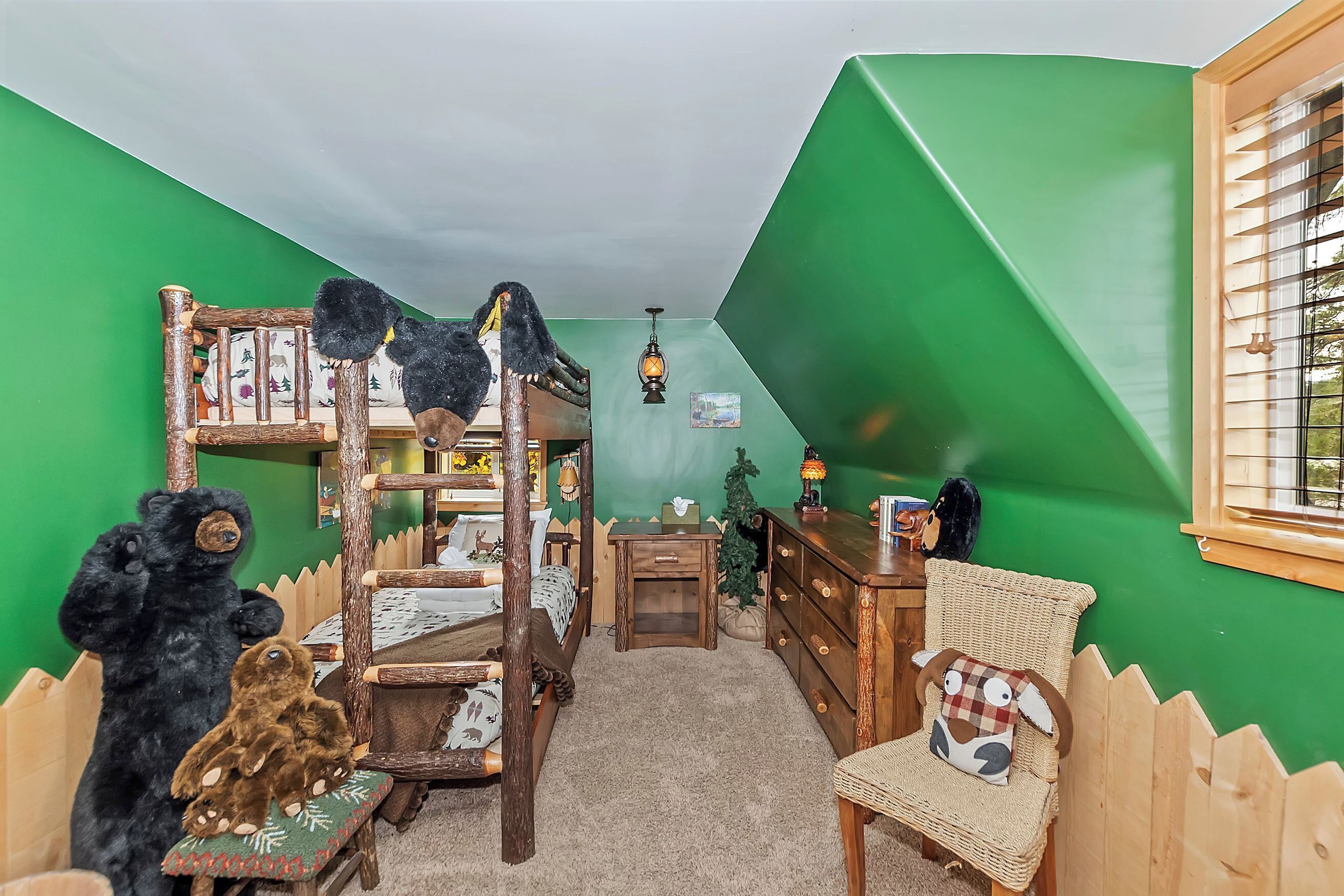 A room with a bunk bed, a dresser, a chair, a small table, and a window with blinds.