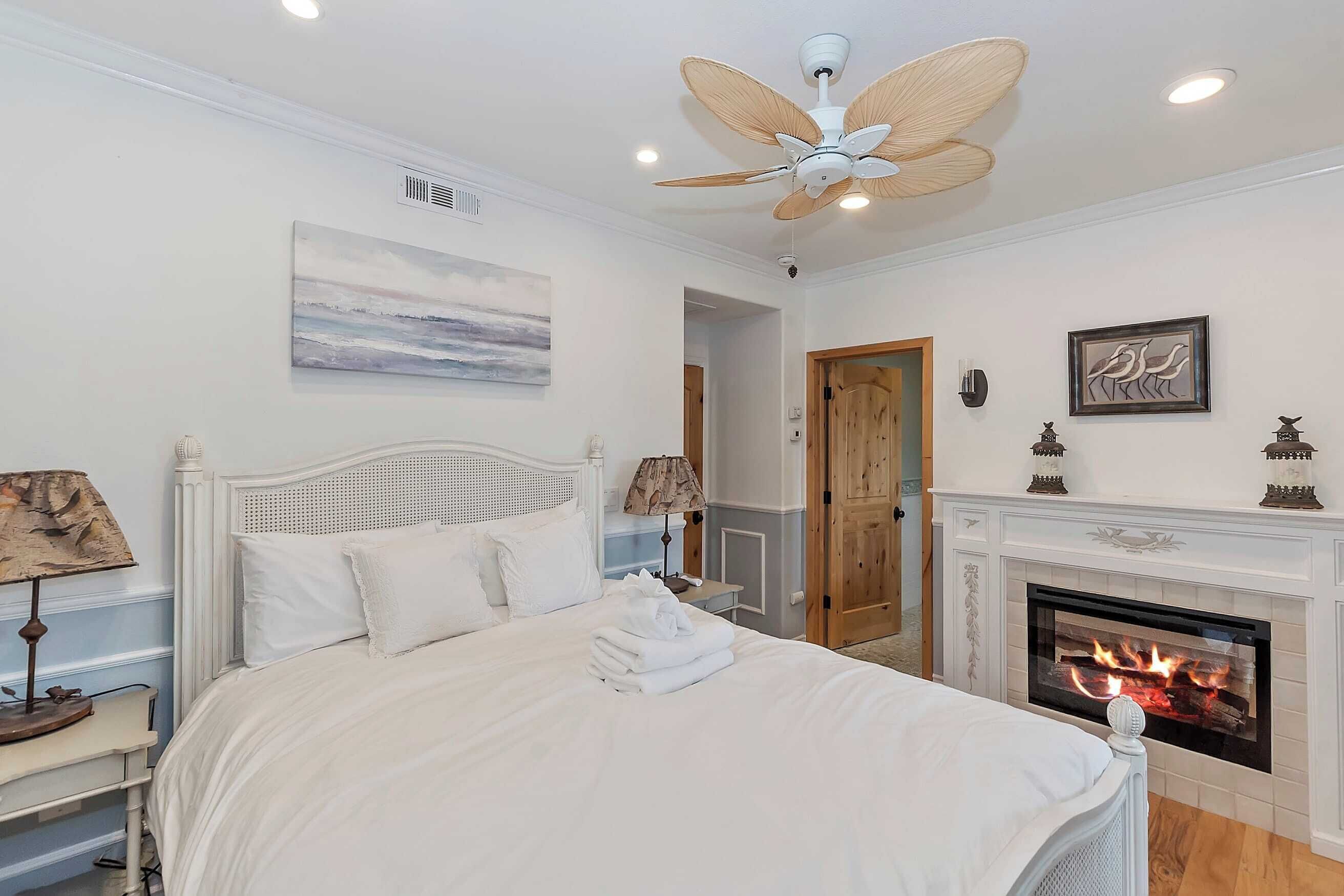 Une chambre à coucher avec un lit, un ventilateur de plafond, une cheminée et un tableau au mur.