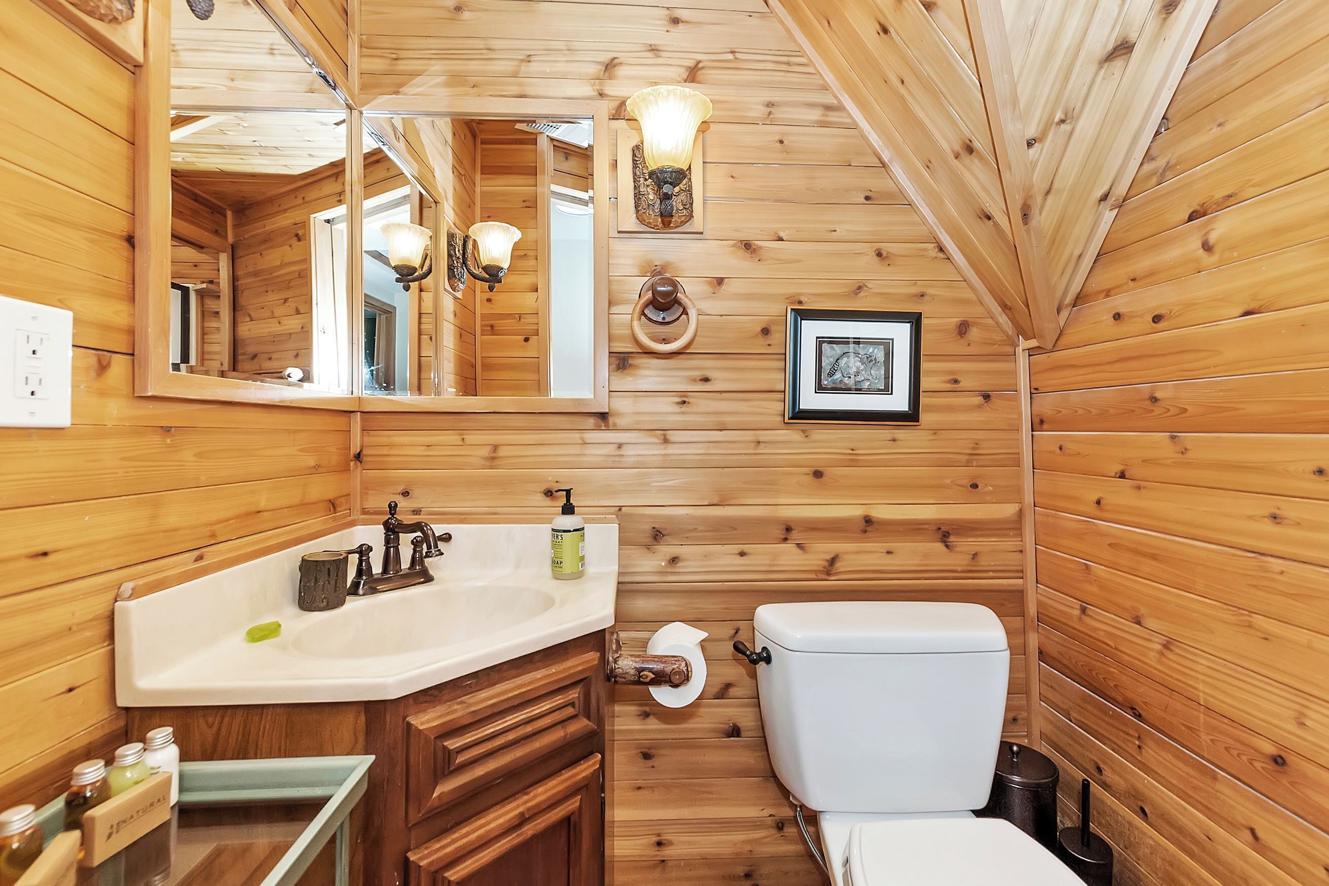 Ein Badezimmer mit Holzvertäfelung, das ein Waschbecken, einen Spiegel, eine Toilette und Wandleuchten umfasst.