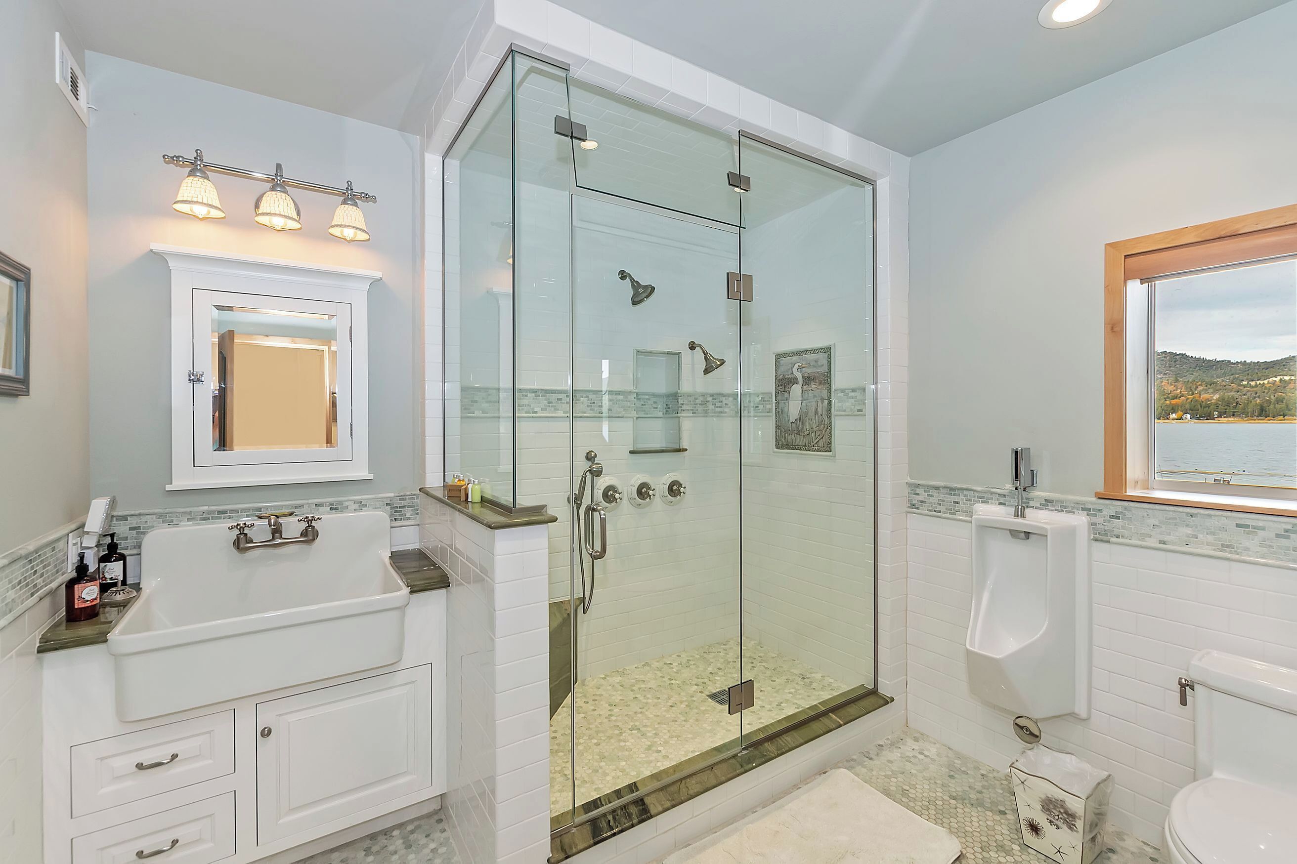 Een moderne badkamer met een douchecabine van glas, een witte wastafel met spiegel en uitzicht op de natuur door een raam.