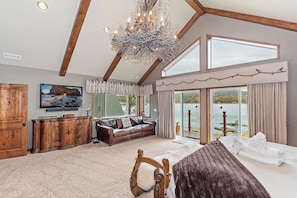 A spacious bedroom with a large bed, a wooden dresser, a leather sofa, and a television. - Lakefront Estate w/ Private Dock, Hottub, Firepit Lagunita Shores by Avantstay (Big Bear Lake)