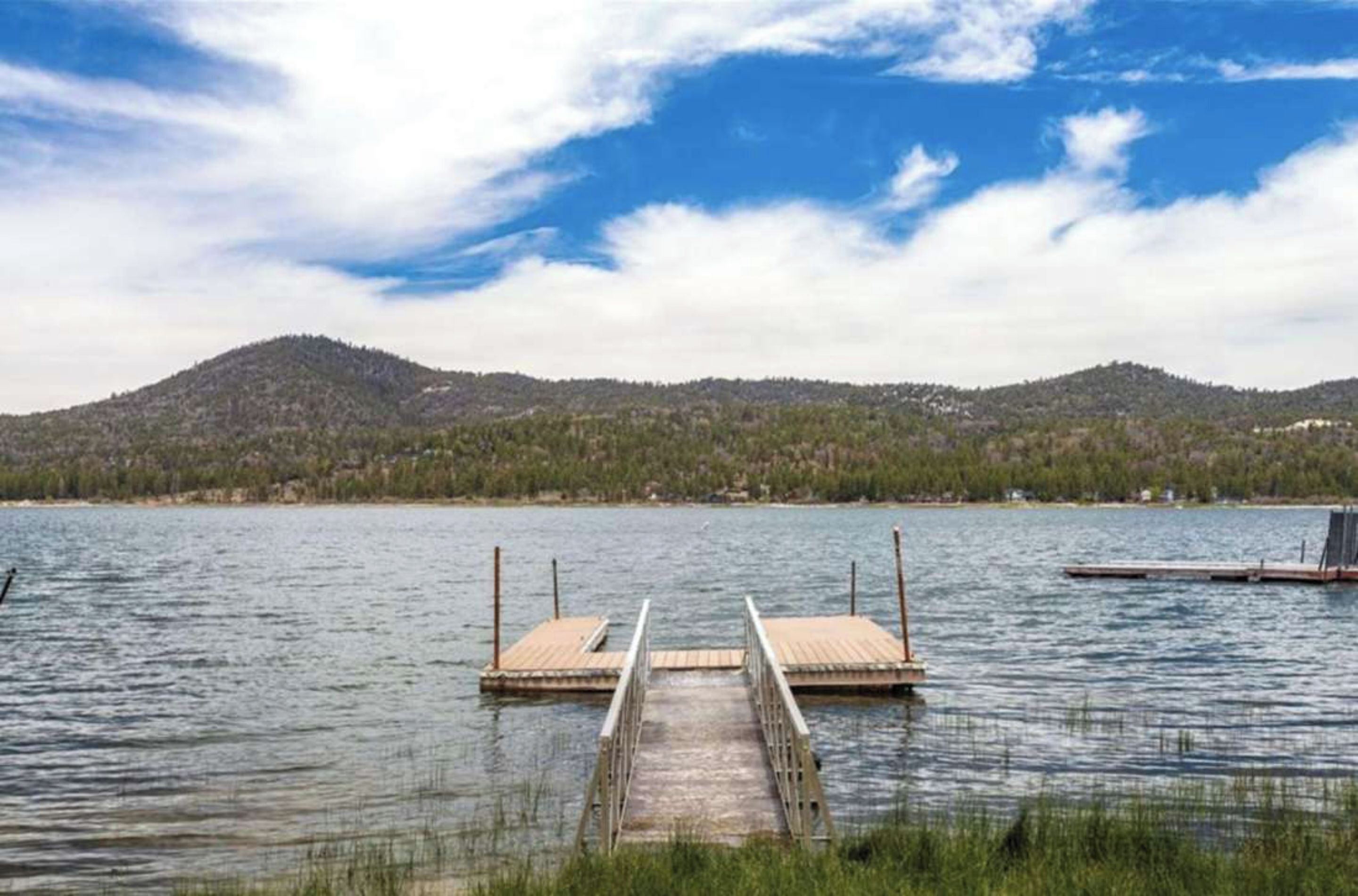 Un lac avec une jetée en bois qui s’avance sur l’eau, entouré de collines et surplombé d’un ciel dégagé.