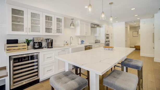 Una cocina moderna con armarios blancos, una isla grande con taburetes y luminarias colgantes.