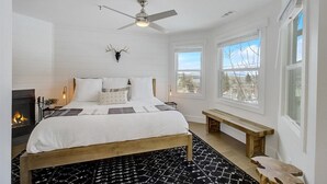 Un dormitorio con cama, ventilador de techo, chimenea, ventana con vistas y un banco.