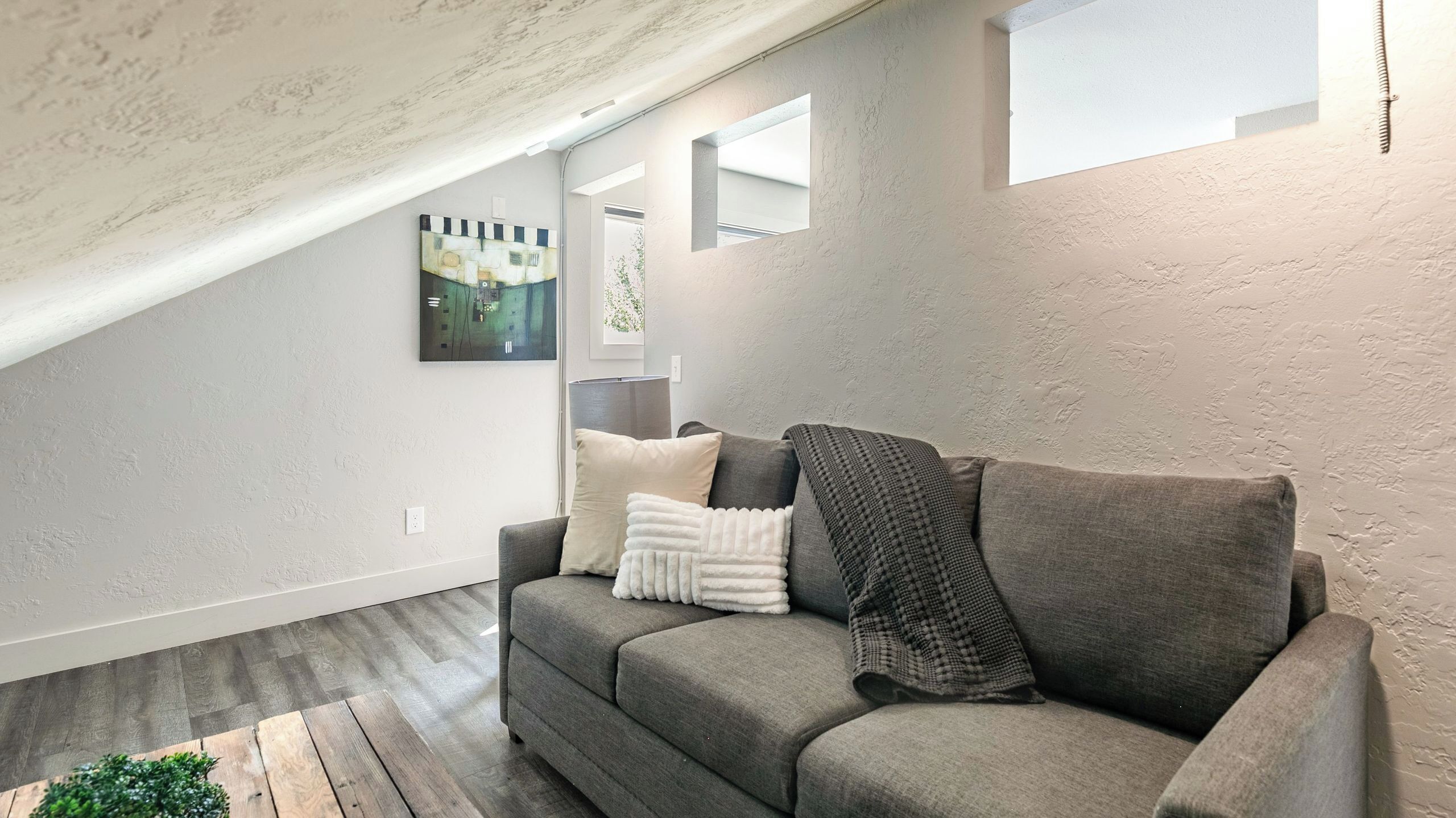 A modern living room with a gray sofa, a small green plant, and a painting on the wall.