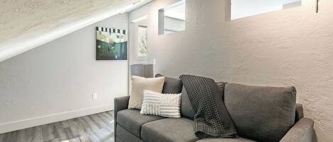 A modern living room with a gray sofa, a small green plant, and a painting on the wall.