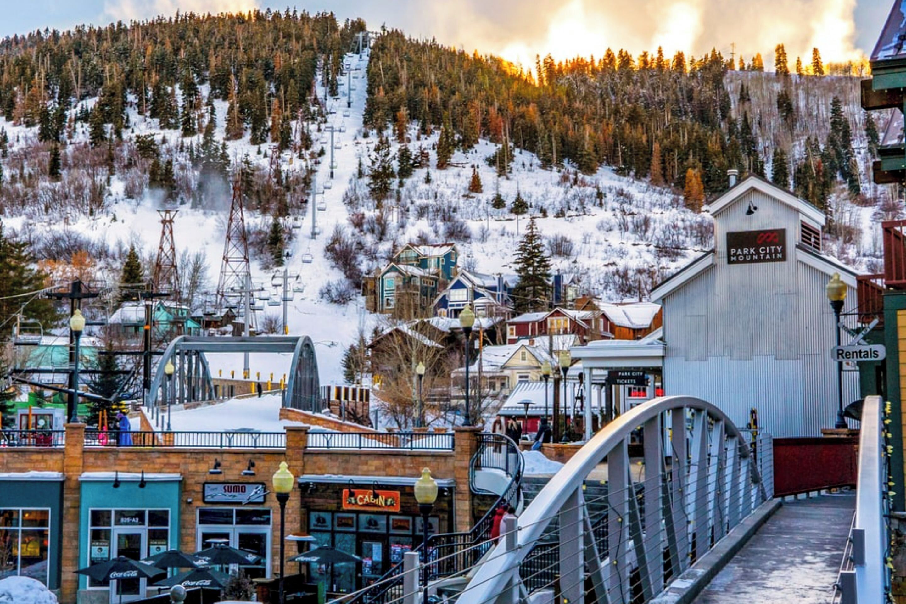 A ski resort town with a mountain backdrop, a bridge, and various buildings including a hotel named 'Park City Mountain'.