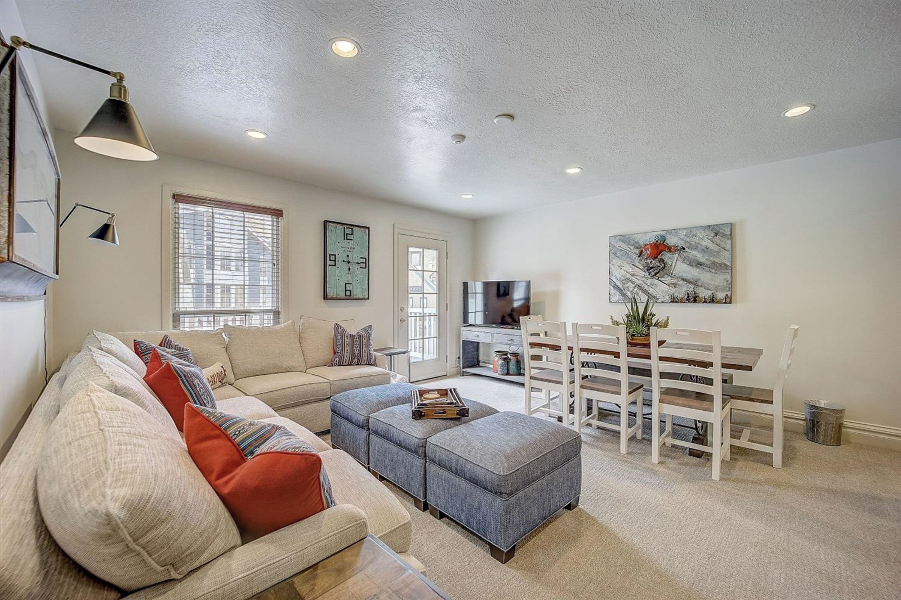 A living room with a sofa, ottoman, dining table, chairs, and a TV.
