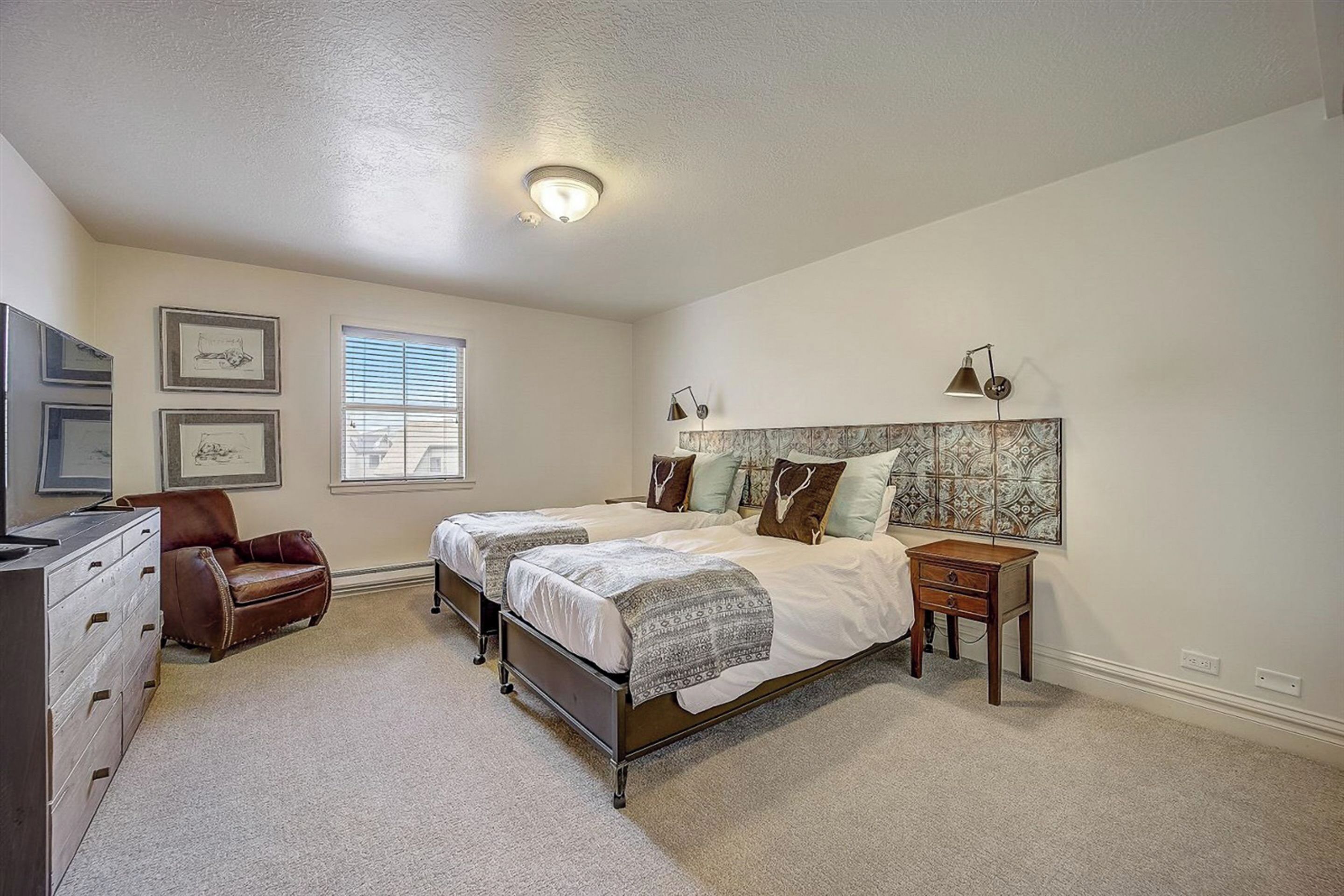 A bedroom with two beds, a dresser, a chair, and a TV.