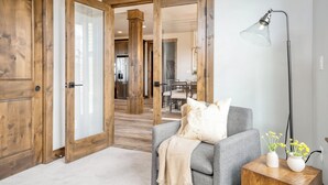 A room with a grey sofa, wooden doors, a lamp, and two vases with flowers.