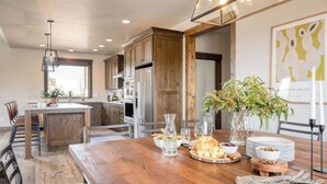 A modern kitchen with wooden cabinets, stainless steel appliances, a wooden dining table, and a vase with flowers.
