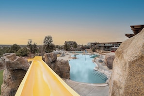 Un parc aquatique avec un toboggan jaune, plusieurs piscines et de gros rochers.