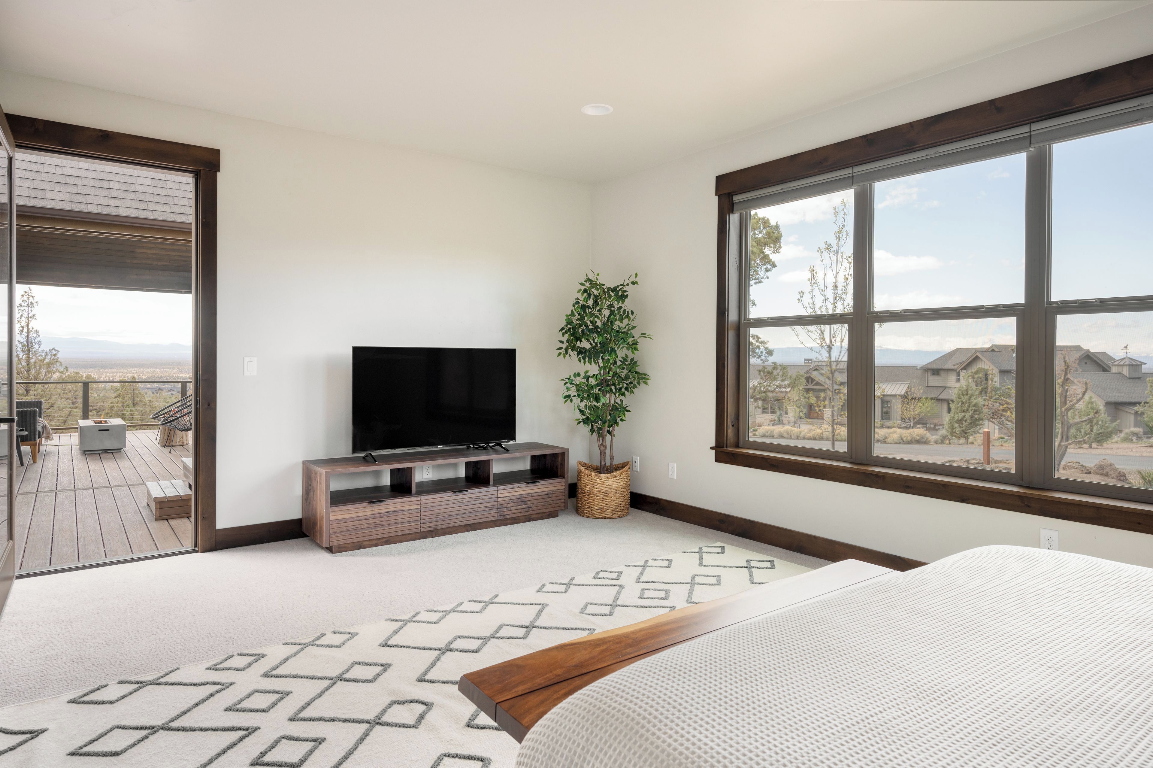 A bedroom with a large window, a TV, a plant, and a view of the outside.