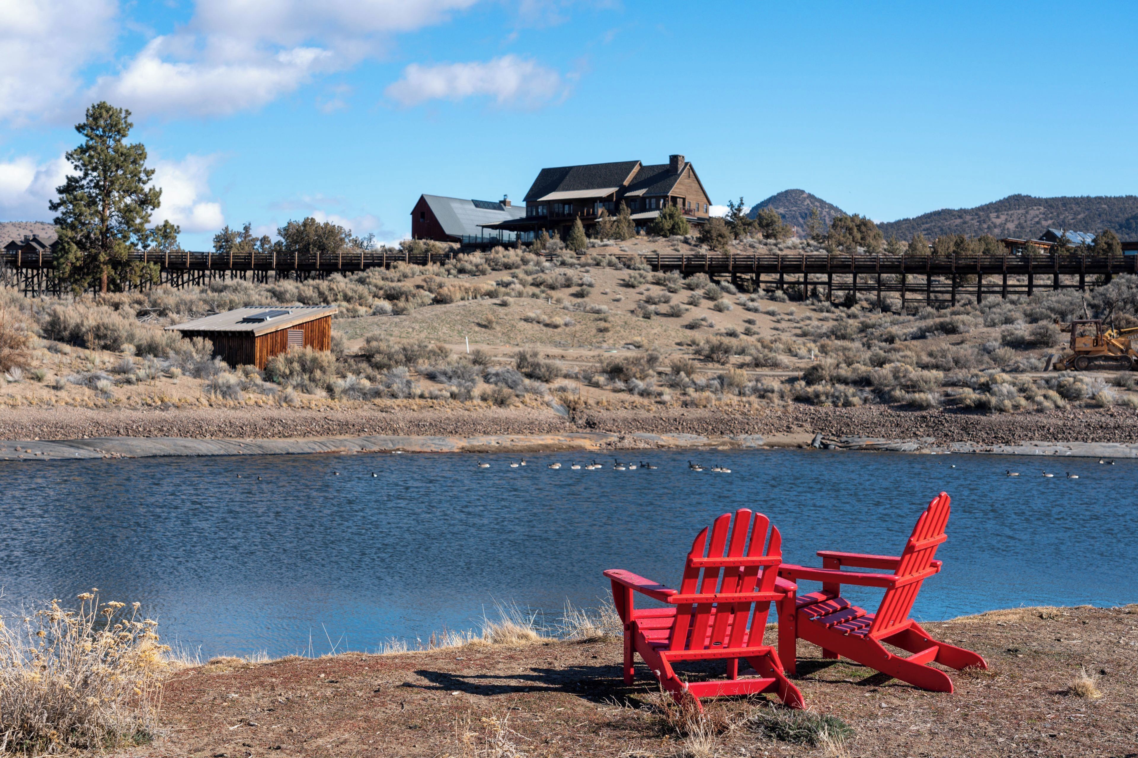A lakeside view with a wooden cabin, a red chair, and a wooden fence.