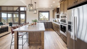 A modern kitchen with a central island, stainless steel appliances, and large windows.
