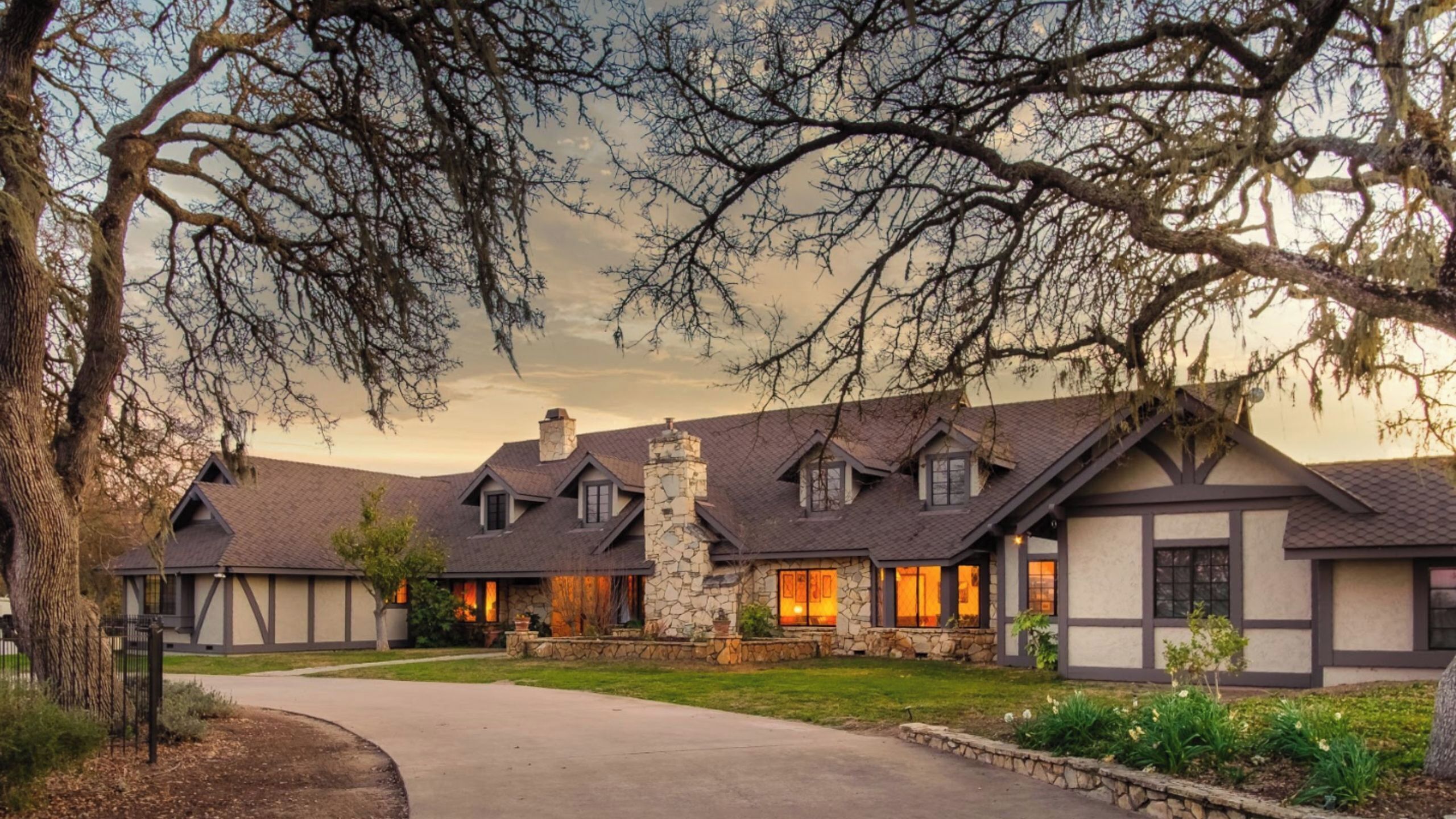A residential building with a stone chimney, multiple gabled roofs, and a driveway leading to the entrance.