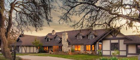 A residential building with a stone chimney, multiple gabled roofs, and a driveway leading to the entrance.