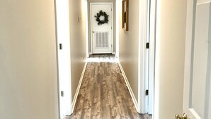 A hallway with wooden flooring, white walls, and a door at the end with a wreath. - LOCATION! | Walk to Stadium and Toomer’s | Cozy 4BR Condo in the Heart of Auburn (Auburn)